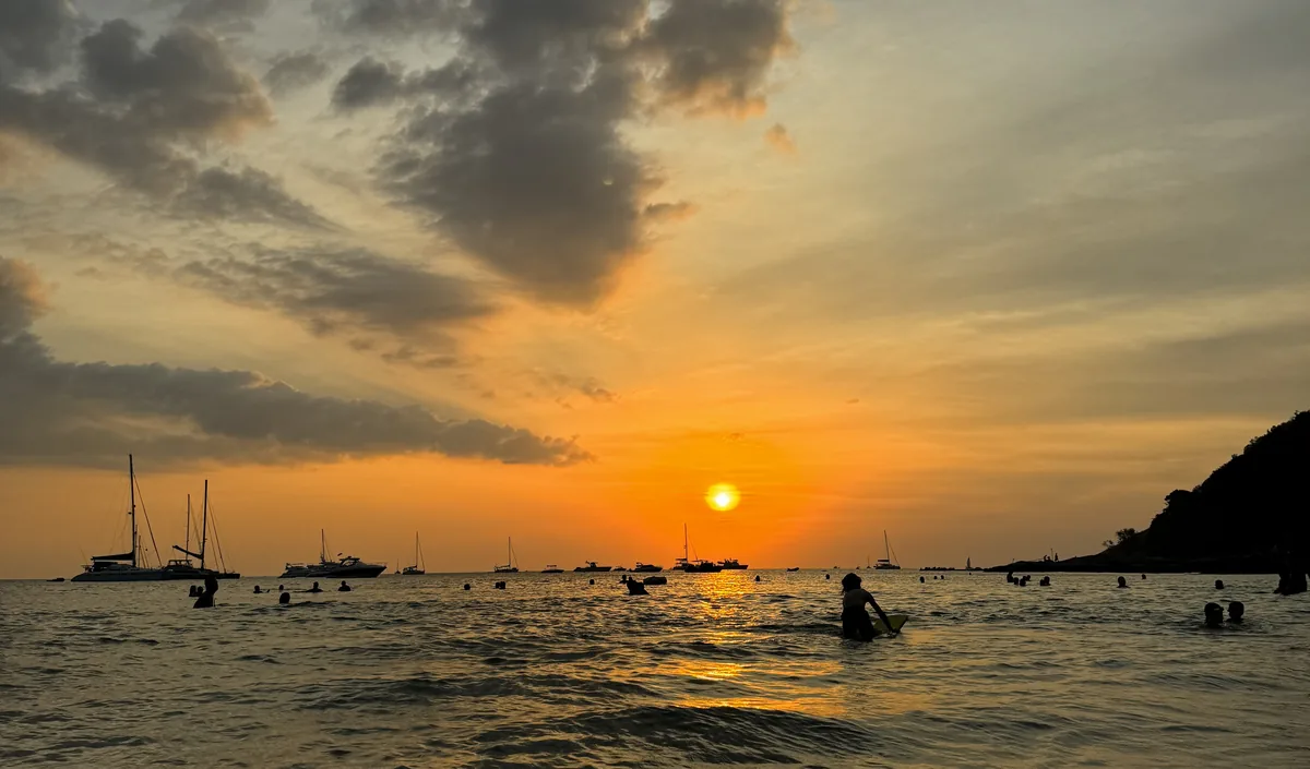 Sunset over the sea with boats and swimmers in silhouette